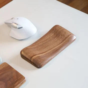 A walnut wood ergonomic mouse wrist rest with rich, dark tones and striking grain patterns, placed on a desk next to a white mouse. The wrist rest, designed for comfortable wrist alignment, enhances workspace aesthetics and reduces strain during long sessions.